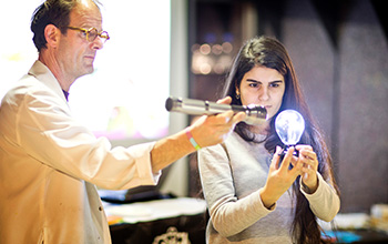 Mad scientist holding flash light point it at a light bulb that a girl is holding