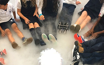Kids sitting in a circle with legs straight out surrounding dry ice and smoke cause from the dry ice.