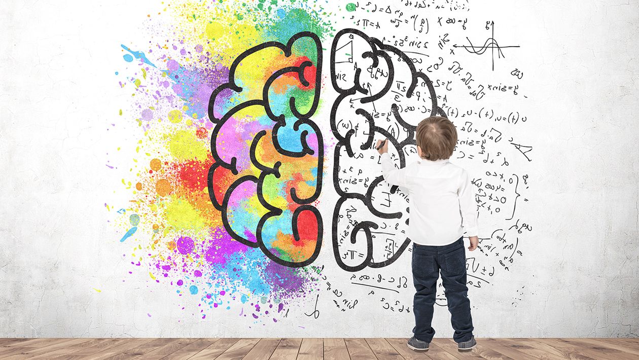 Boy writing formulas on a white wall with a brain and color splashes on it.